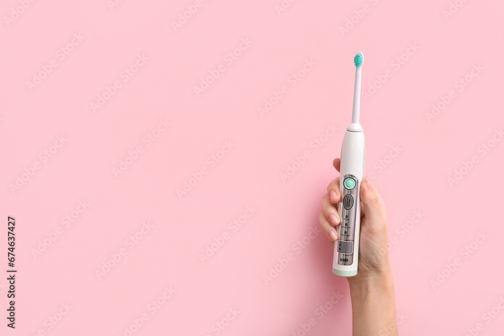 Female hand with electric toothbrush on pink background. - obrazy, fototapety, plakaty 