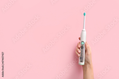 Female hand with electric toothbrush on pink background. photo