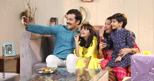 Indian young family  of four celebrating Raksha Bandhan festival with sweet laddoo, oil  lamp or diya taking selfie
