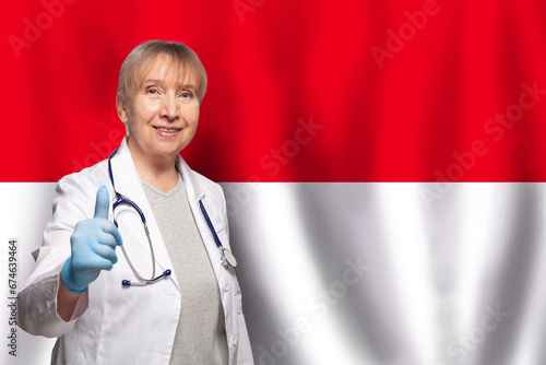 Indinezian smiling mature doctor woman holding stethoscope on flag of Indinezian background photo
