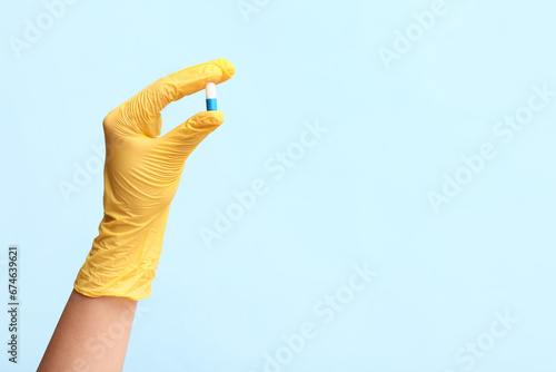 Hand of doctor in yellow glove with pill on blue background