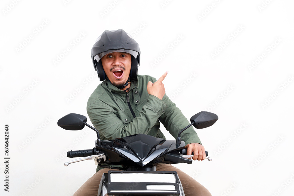 Excited asian man pointing sideways while riding motorcycle. Isolated on white background Excited asian man pointing sideways while riding motorcycle. Isolated on white background