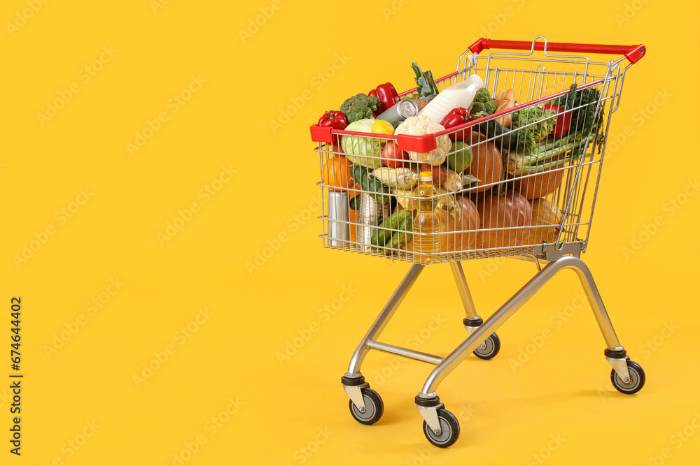 Shopping cart full of food on yellow background Shopping cart full of food on yellow background