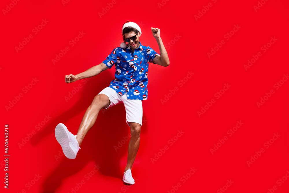 Full size photo of funky young man dancing have fun wear santa claus print x-mas clothes isolated on red color background
