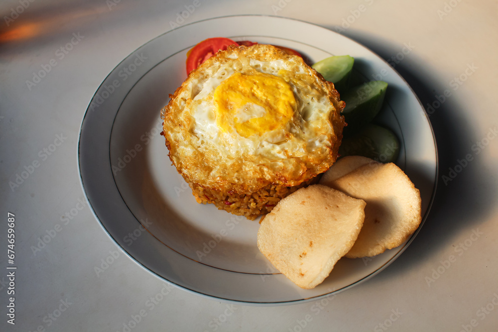 Indonesian style spicy fried rice with shredded chicken, cucumber pieces and tomato pieces and fried eggs and shrimp crackers.