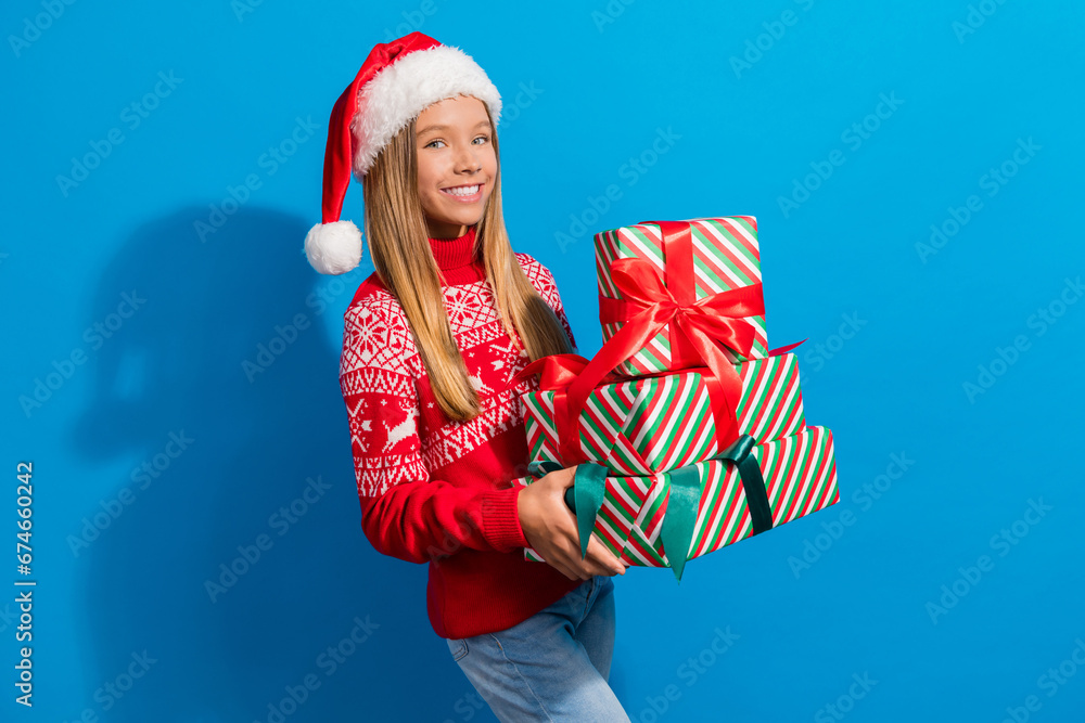 Obraz premium Photo of toothy beaming schoolgirl with blond hair dressed red sweater holding gift boxes on christmas isolated on blue color background