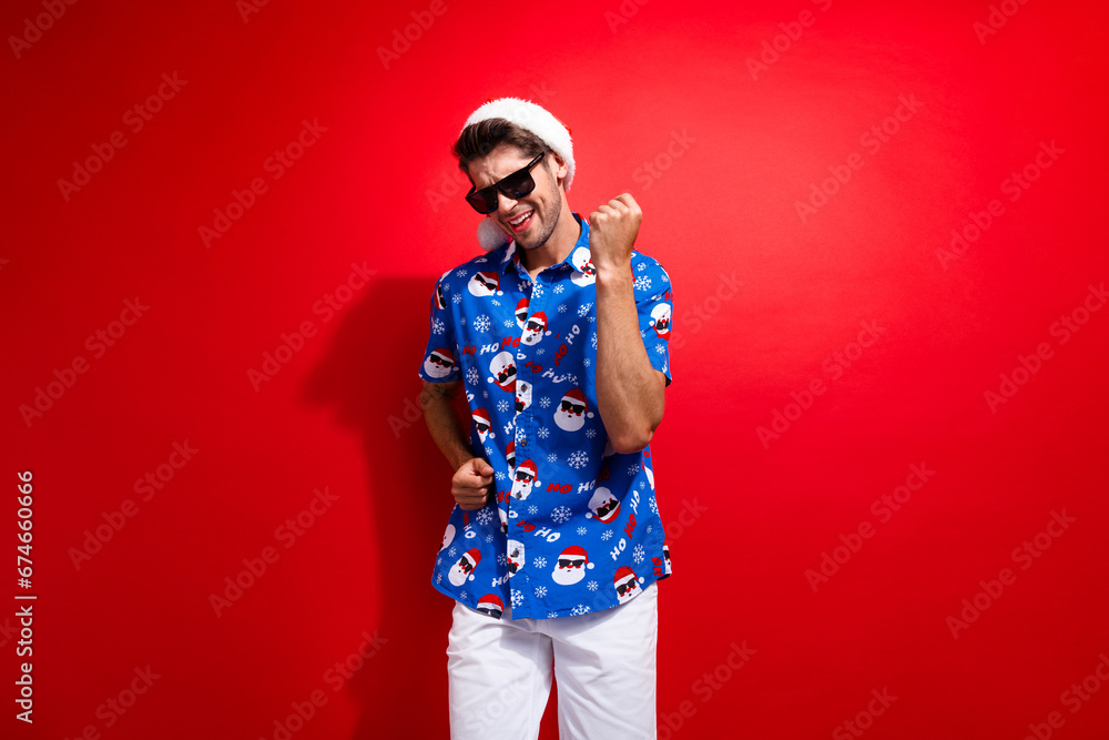 Photo of funny young man xmas vibe wear traditional santa print shirt with hat dancing on new year party isolated over red color background