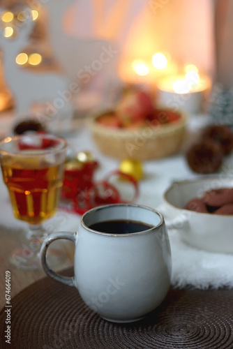 Cup of tea or coffee  glass of wine or juice  bowl of cookies  organic pomegranate  fluffy blanket  pine cones  various Christmas decorations and lit candles on the table. Christmas hygge concept.