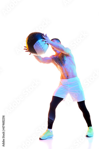 Fototapeta Naklejka Na Ścianę i Meble -  Athletic young man with strong, muscular body training with fitness ball against white studio background in neon light. Concept of sport, active and healthy lifestyle, body care, fitness