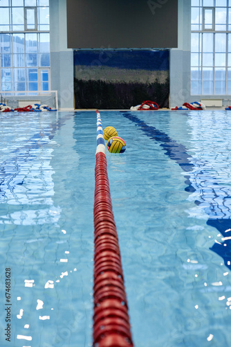 Long red plastic buoy representing finish line on surface of blue water in swimming pool and two balls on background prepared for game photo