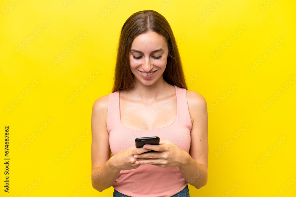 Young caucasian woman isolated on yellow background sending a message or email with the mobile Young caucasian woman isolated on yellow background sending a message or email with the mobile