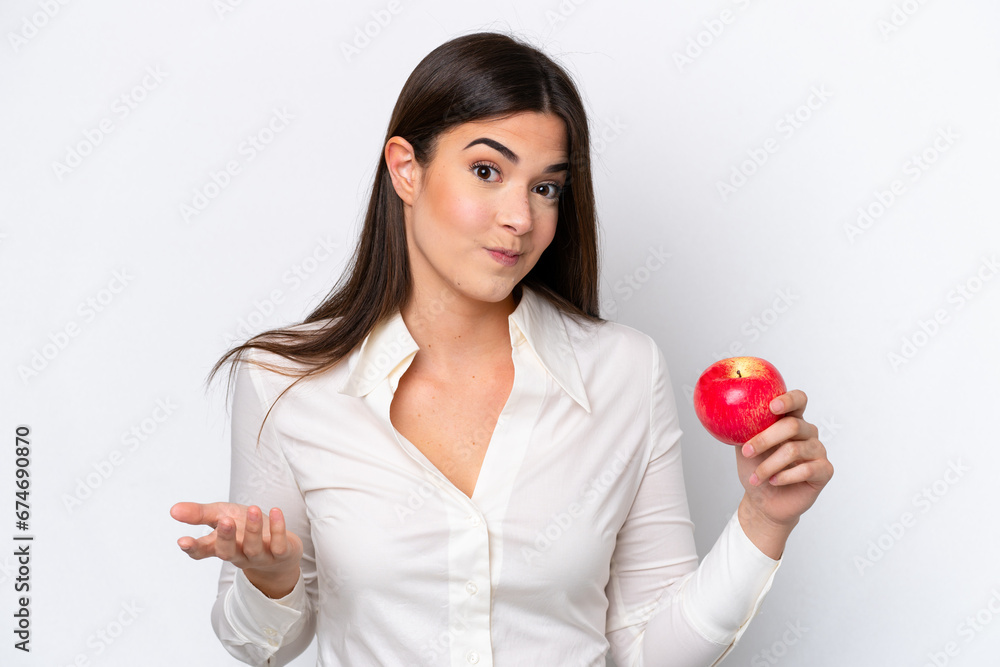 Young Brazilian woman with an apple isolated on white background making doubts gesture while lifting the shoulders Young Brazilian woman with an apple isolated on white background making doubts gesture while lifting the shoulders
