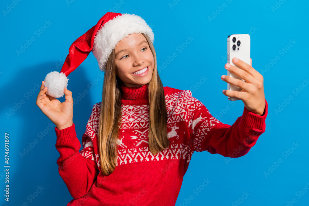 Photo of beautiful schoolgirl with blond hair dressed red sweater make selfie on smartphone touch pompom isolated on blue color background Photo of beautiful schoolgirl with blond hair dressed red sweater make selfie on smartphone touch pompom isolated on blue color background