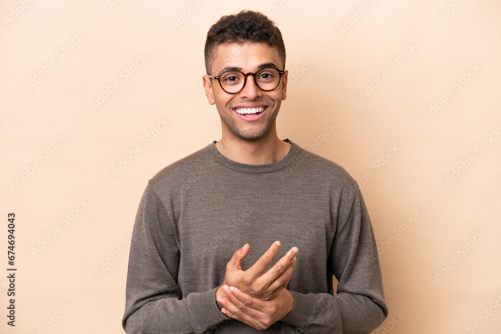 Young Brazilian man isolated on beige background laughing - obrazy, fototapety, plakaty 