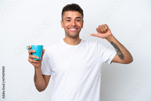 Young Brazilian man holding cup of coffee isolated on white background proud and self-satisfied