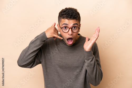 Young Brazilian man isolated on beige background making phone gesture and doubting