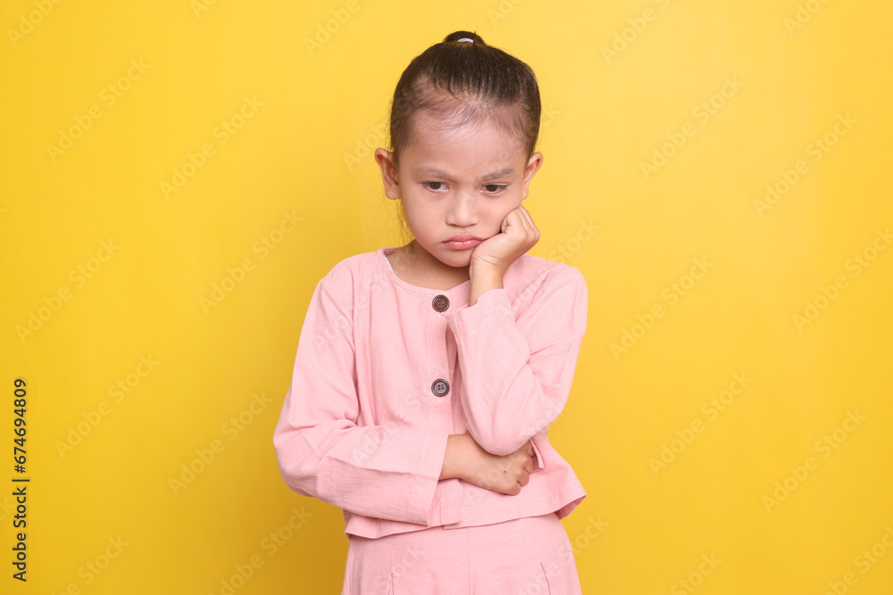 Sad Asian little girl looking down and feeling sad isolated over yellow background Sad Asian little girl looking down and feeling sad isolated over yellow background