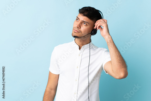 Telemarketer Colombian man working with a headset over isolated background having doubts