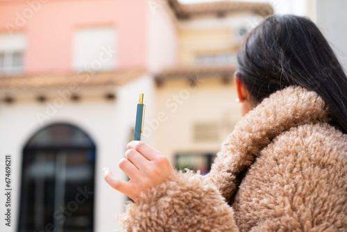 Young woman holding a pen at outdoors in back position