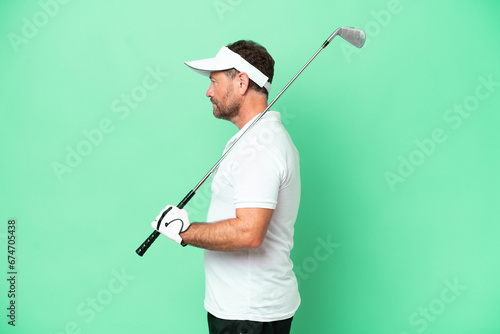 Middle age caucasian man isolated on green background playing golf in lateral position