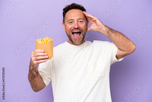 Middle age caucasian man holding fried chips isolated on purple bakcground with surprise expression © luismolinero