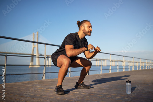 young caucasian man enjoys outdoor fitness workout squats at pier © Prostock-studio