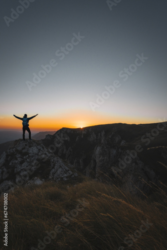 A happy male traveler celebrating a successful completed hiking route on the mountain top at sunset or sunrise adventure travel.