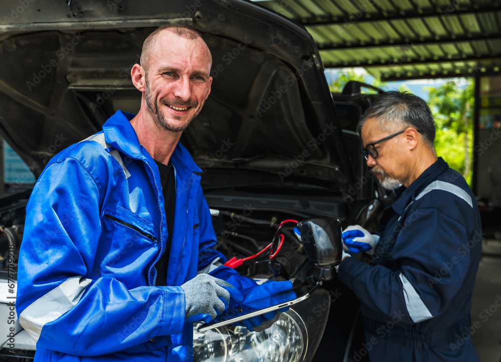 Smiling Caucasian auto mechanic man working on car with senior technician teammate in auto repair Smiling Caucasian auto mechanic man working on car with senior technician teammate in auto repair