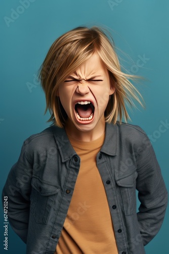 Angry irritated girl. Full of rage. Emotional portrait of an upset preteen boy screaming in anger. Requirements for parents. Wrong perception. Hysterics. Photo on blue background.