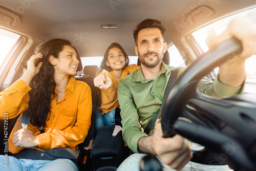 Joyful family moment in car, dad touching steering wheel, daughter points