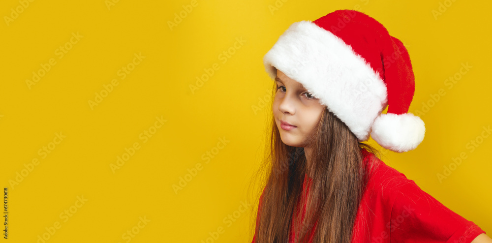 Pensive little girl wearing Christmas costume and Santa hat standing isolated over yellow background wall in studio Pensive little girl wearing Christmas costume and Santa hat standing isolated over yellow background wall in studio