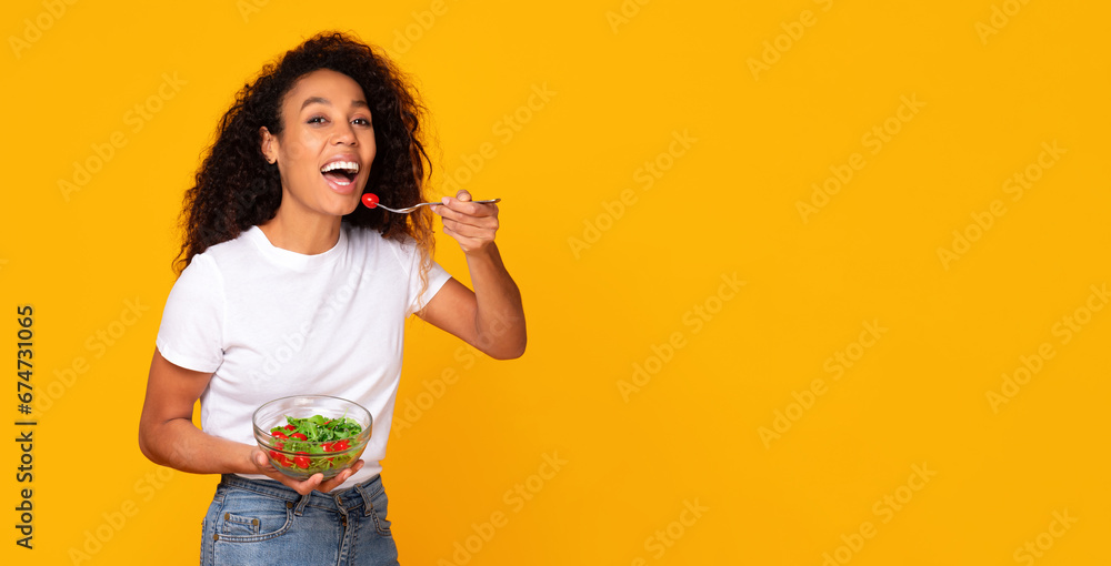 Young African American woman enjoying green salad over yellow background Young African American woman enjoying green salad over yellow background