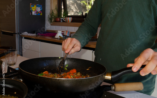 person cooking stir fry vegetables in wok with wooden spoon