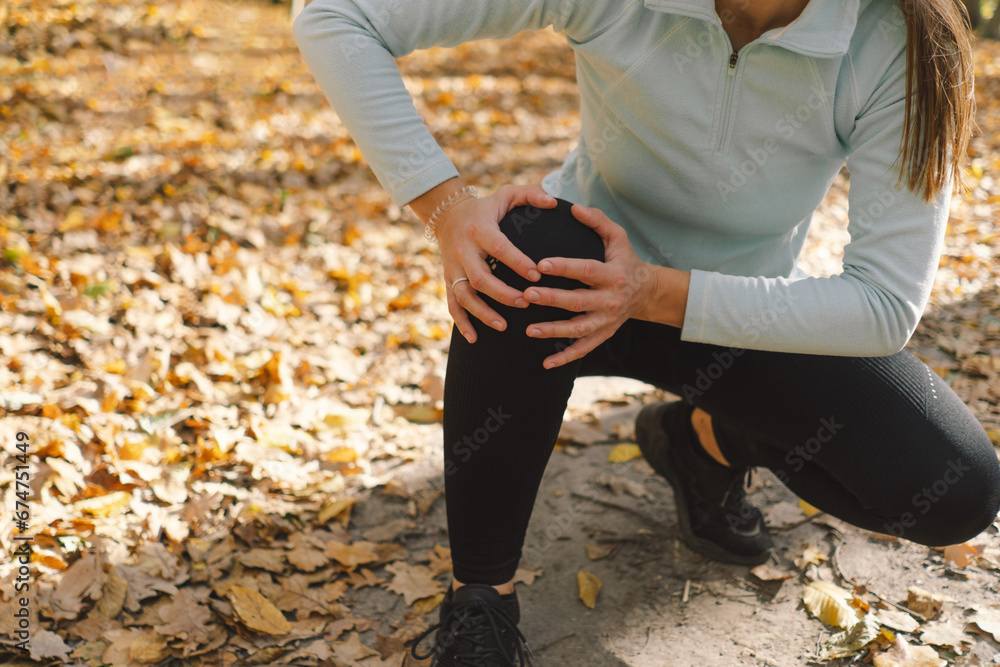 Fototapeta premium The girl suffers from pain, spasm sprain of the knee during outdoor training in the autumn forest