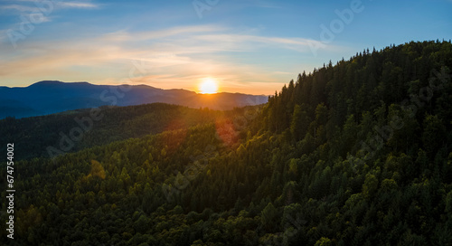 Aerial view of amazing scenery with dark mountain hills covered with forest pine trees at autumn sunrise. Beautiful wild woodland at dawn