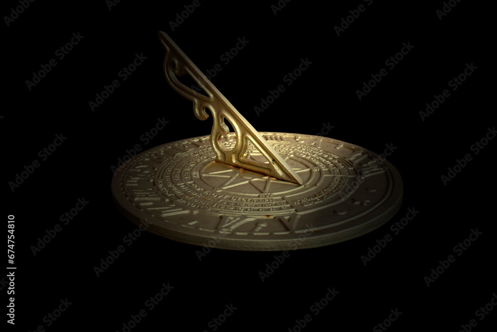 Antique brass sundial with time and calendar engraved on the surface. Isolated on black background