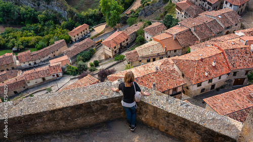 Tourist woman contemplating the rooftops of the medieval village from the top of the wall, Frias, Burgos.