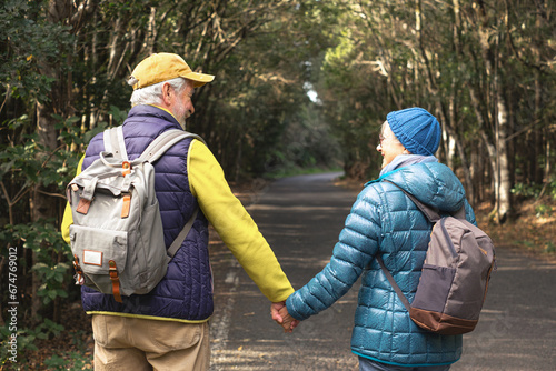 Carefree smiling senior couple holding backpack walking in national park in La Gomera. Elderly active man and woman hiking in mountain forest enjoying nature and healthy lifestyle