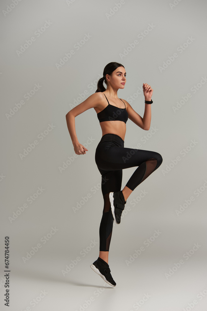 young fit woman in active wear stepping on place while doing cardio exercise on grey background young fit woman in active wear stepping on place while doing cardio exercise on grey background