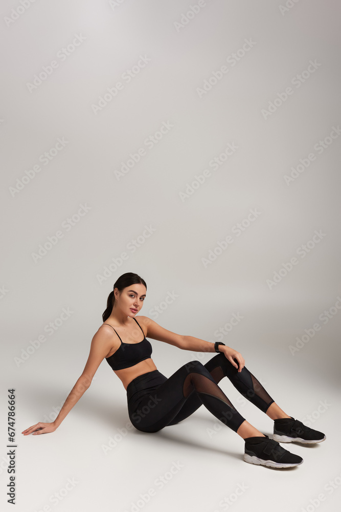 tired sportswoman in black active wear with fitness tracker on wrist resting on grey backdrop tired sportswoman in black active wear with fitness tracker on wrist resting on grey backdrop