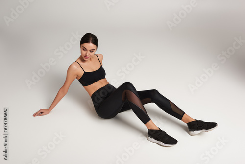 attractive sportswoman in black active wear with fitness tracker on wrist resting on grey backdrop © LIGHTFIELD STUDIOS