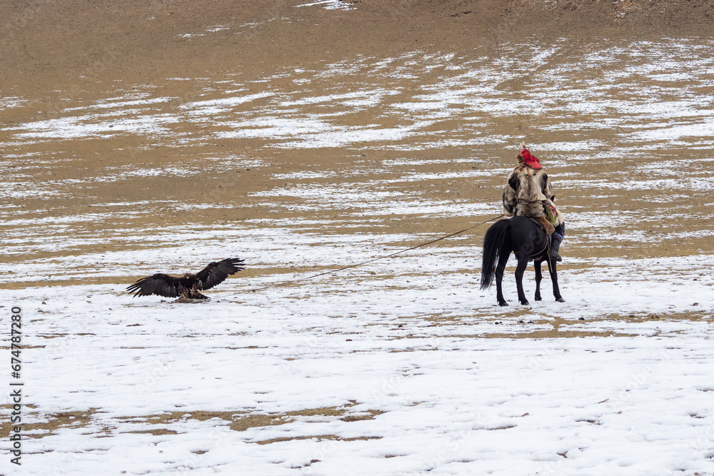 A male hunter on a horse with his back to the camera trains a golden eagle. Eagle hunters are people who train and hunt with golden eagles in Mongolia. A traditional sport in Kazakhstan and Mongolia.