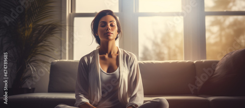 A woman practicing meditation, yoga, relaxation on her comfortable sofa in her calm and cosy home, with tranquility, peaceful mind, wellbeing and serenity photo