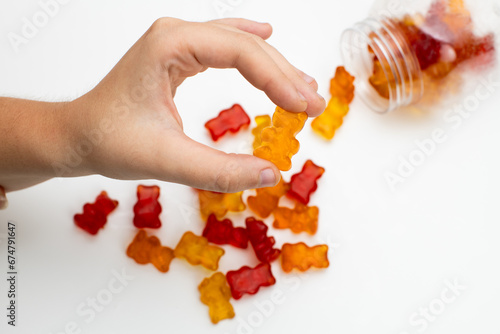 Child taking gummy bear candy from glass jar on yellow background, closeup