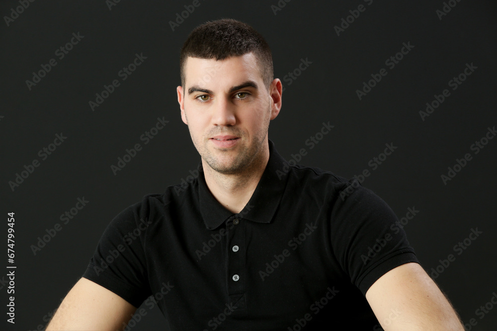 Fototapeta premium Studio portrait of young man in black polo shirt on the black background