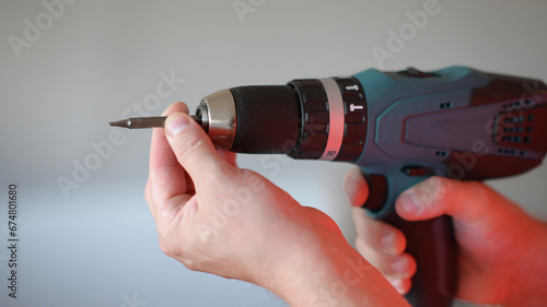a man holds a drill in his hand and places the surface of the bit for screwing on a white background. photo