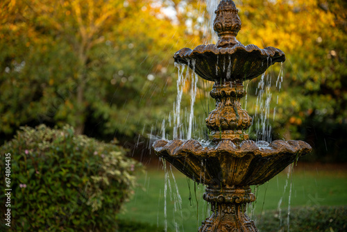 Fountain in a park with the setting sun illuminating the background trees. Detail view.
