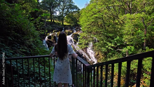 Beautiful woman visits Rhaeadr Ewynnol Swallow Falls Waterfall, Tourist attraction in Wales. Female tourist looking at the churning waterfalls in a picturesque, wooded setting in Wales. photo