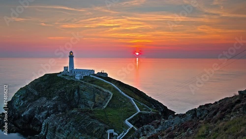 Timelapse over South Stack Lighthouse at golden sunset in north-west coast of Holy Island, Wales. Hyperlapse over Lighthouse with steps and picturesque footbridge over the wild Atlantic ocean. photo