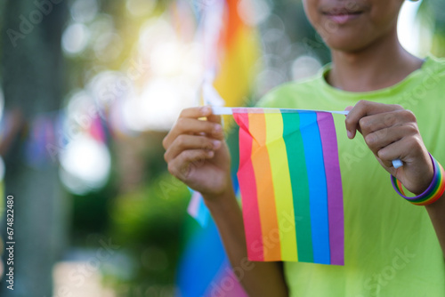 Celebrating LGBTQ pride month with flag closeup, young asian kid happy smiling with nature background. Embracing lesbian, gay, bisexual, transgender, and queer communities.